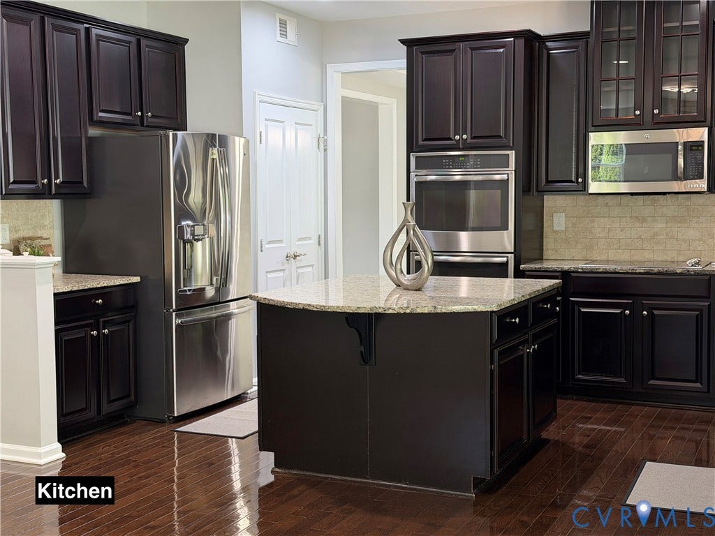 Kitchen featuring dark cabinetry, stone-surface countertops, central island, stainless steel appliances, and wood-finish flooring