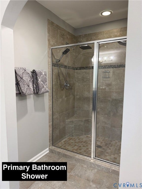 Walk-in shower featuring tile surround with decorative accent inlay, built-in corner bench, dual shower heads, and a glass enclosure