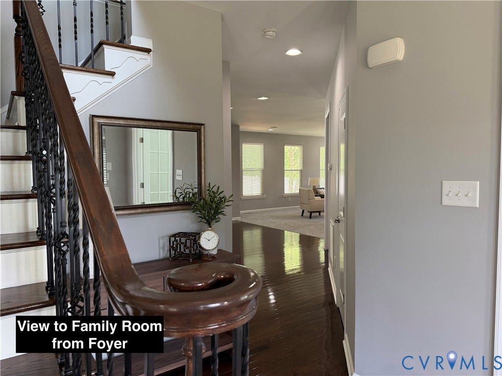Foyer featuring wood-finish flooring, a staircase with a stained wood handrail, and intricate wrought iron balusters