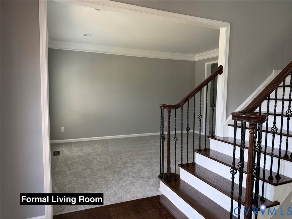 Staircase featuring wood treads, white risers, and decorative metal balusters with a wood handrail, paired with neutral carpeting and crown molding