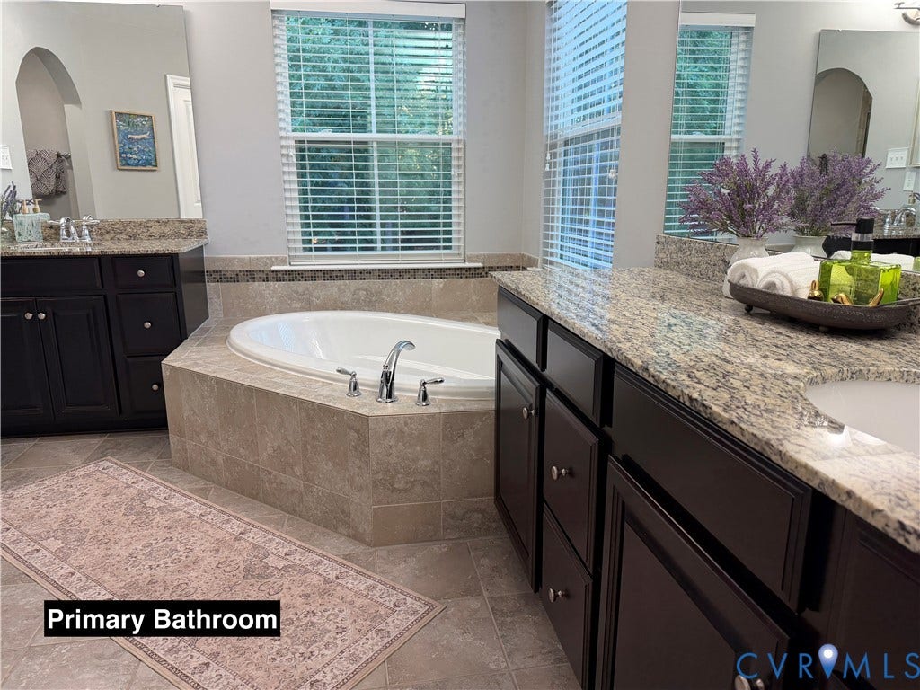Built-in dark wood cabinetry with stone countertops, undermount sinks, and a deep soaking tub featuring tiled surround