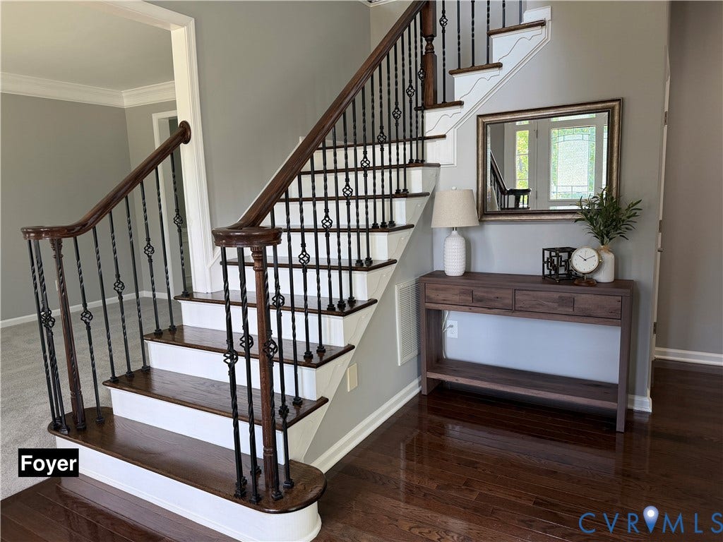 Staircase featuring dark wood-finish treads and handrails with decorative black metal balusters, polished dark wood-finish flooring, and crown molding