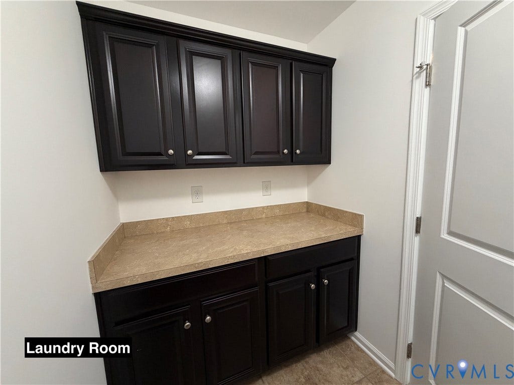 Utility room featuring dark-finish upper and lower cabinetry, integrated neutral-toned countertop with backsplash, and tile flooring