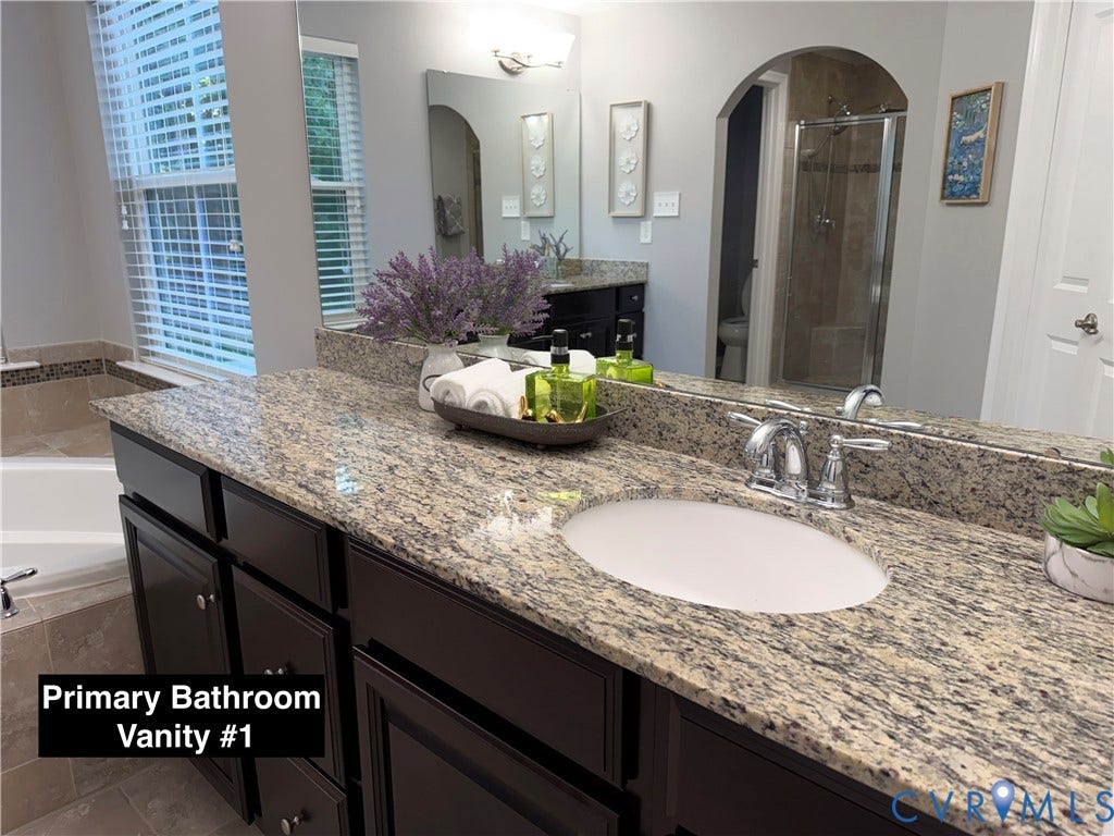 Dark-toned cabinetry vanity with a stone countertop, undermount oval sink, chrome dual-handle faucet, and full-width vanity mirror