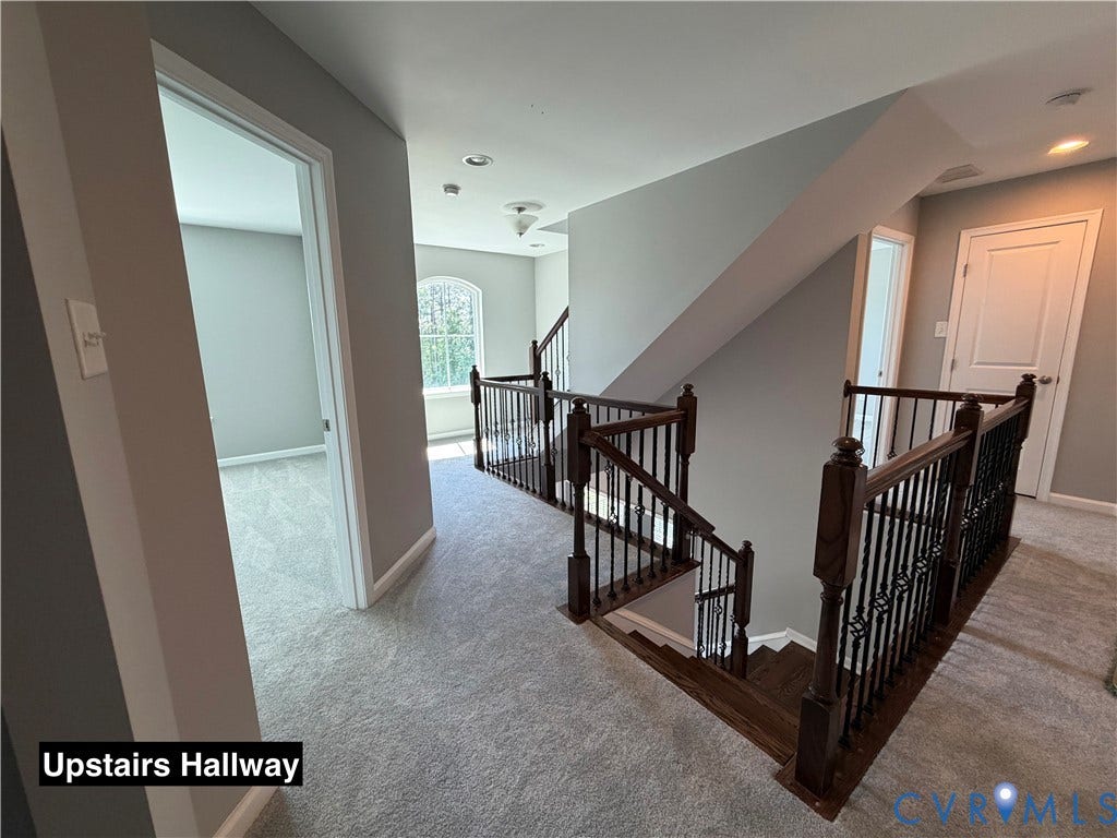 Staircase featuring wood handrails, dark metal balusters, arched window, and neutral wall-to-wall carpeting