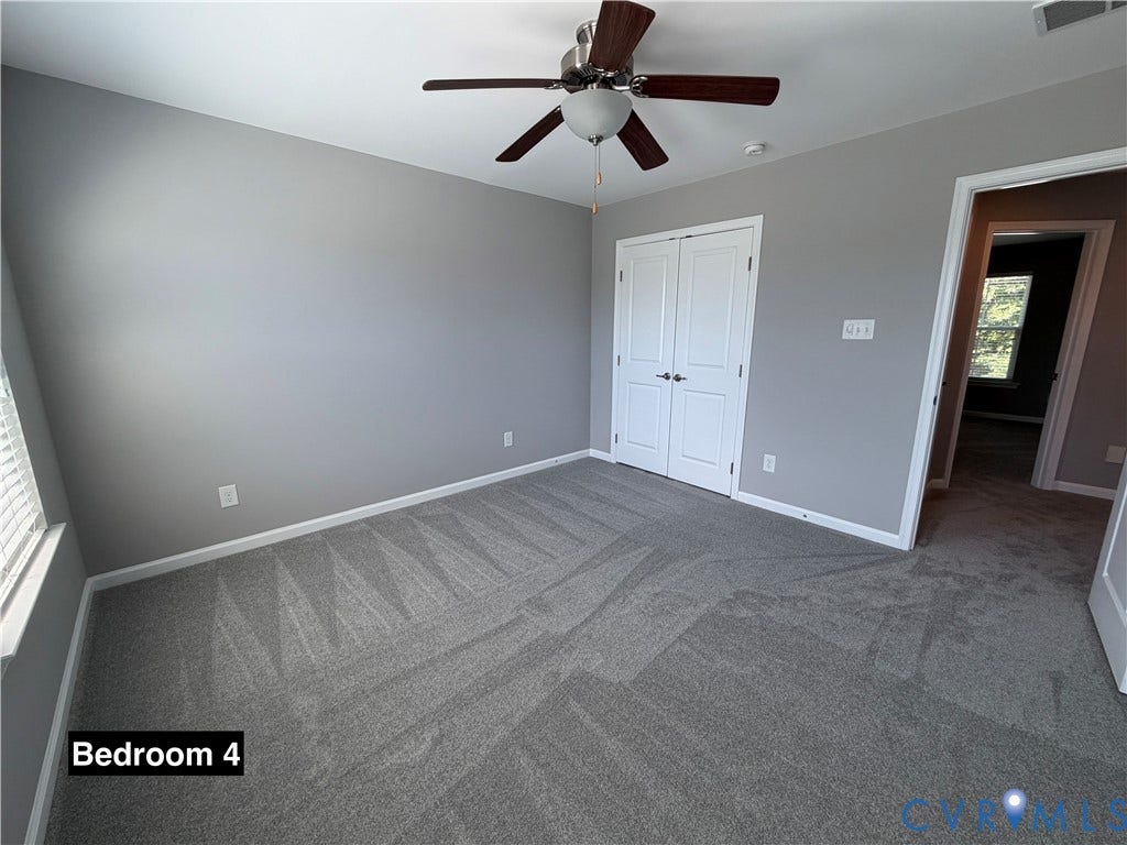 Neutral-toned walls, wall-to-wall carpeting, ceiling fan with light fixture, and double-door reach-in closet