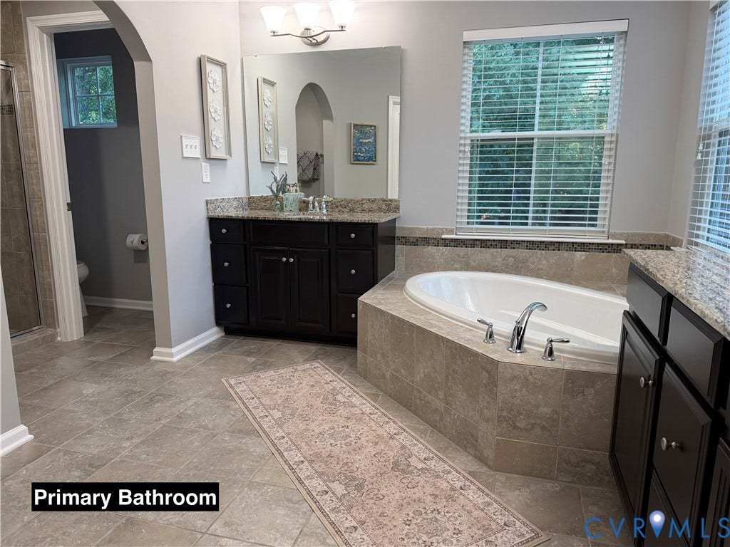 Bathroom featuring a deep soaking tub with a tiled surround, dual dark-finish cabinetry, stone-surface countertops, and tile flooring