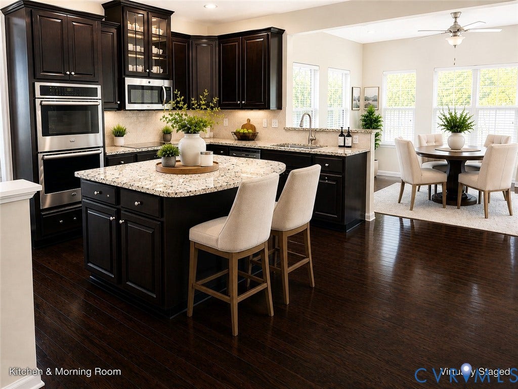 Chef's kitchen featuring dark cabinetry with glass-front upper cabinets, stainless steel double wall ovens and microwave, granite-topped island with seating for two, and matching granite countertops throughout and seamless flow between the kitchen and adjoining morning room.