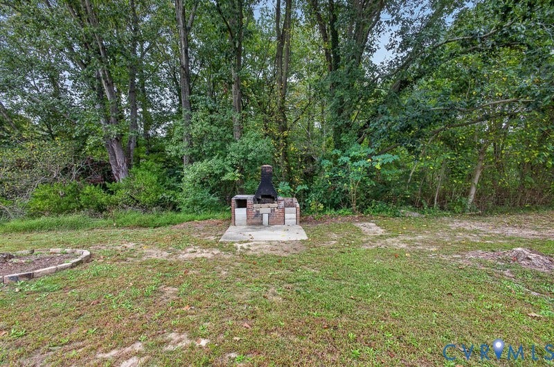Backyard area featuring a permanent brick masonry grill, concrete base, and curved stone garden border against a backdrop of mature trees