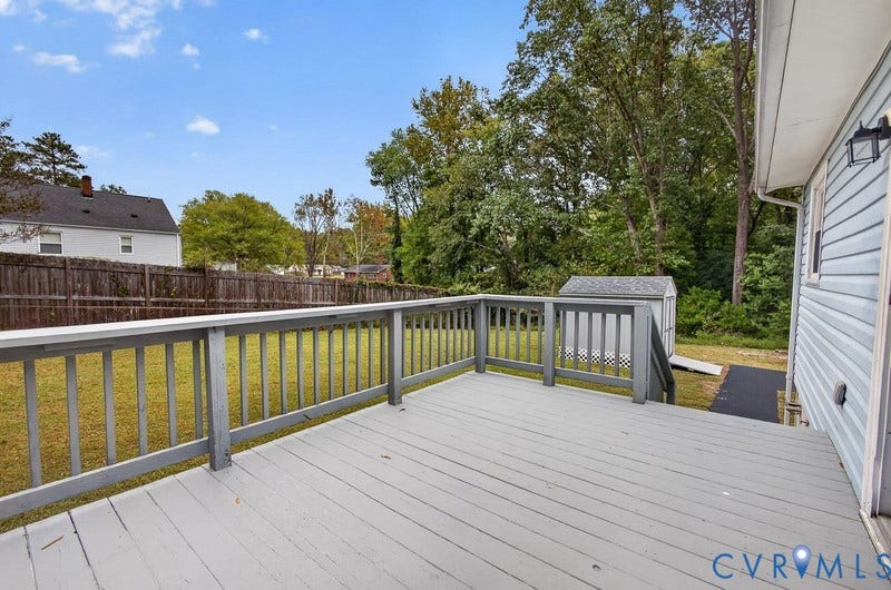 Elevated wood deck with painted railings, fenced backyard, and a detached storage structure
