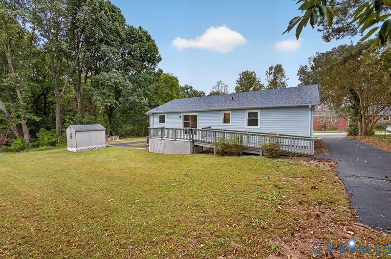 Exterior of the residence featuring horizontal siding, asphalt shingle roofing, an elevated wood deck with a ramp, a detached storage structure, and paved driveway
