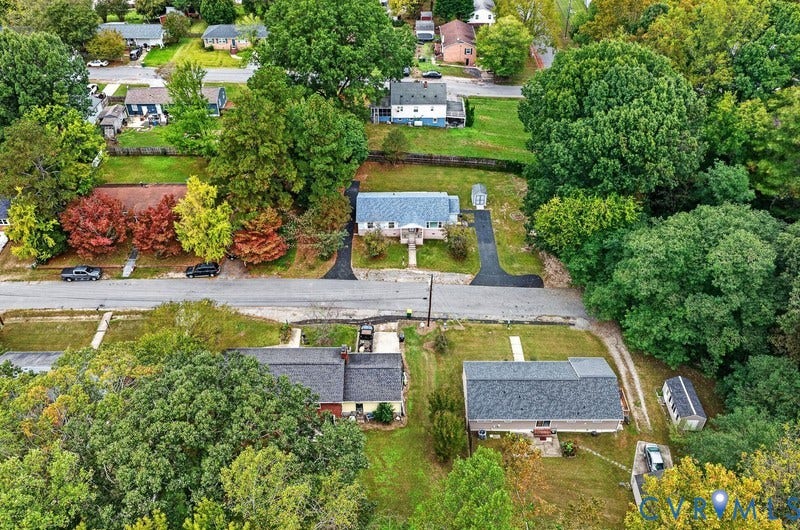 Aerial perspective of a residential property featuring an asphalt driveway, detached storage structure, and expansive lot with mature trees