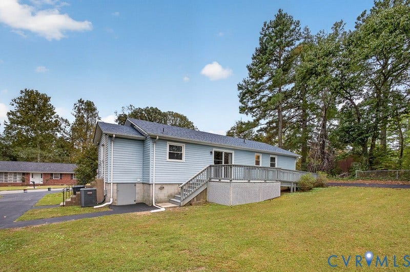 Exterior siding, elevated wood deck with railing, asphalt driveway, and expansive grass yard