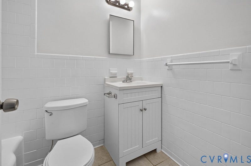 White subway tile wall cladding, beadboard-style vanity cabinet, light-toned stone-finish countertop, rectangular vanity mirror, and three-bulb vanity lighting