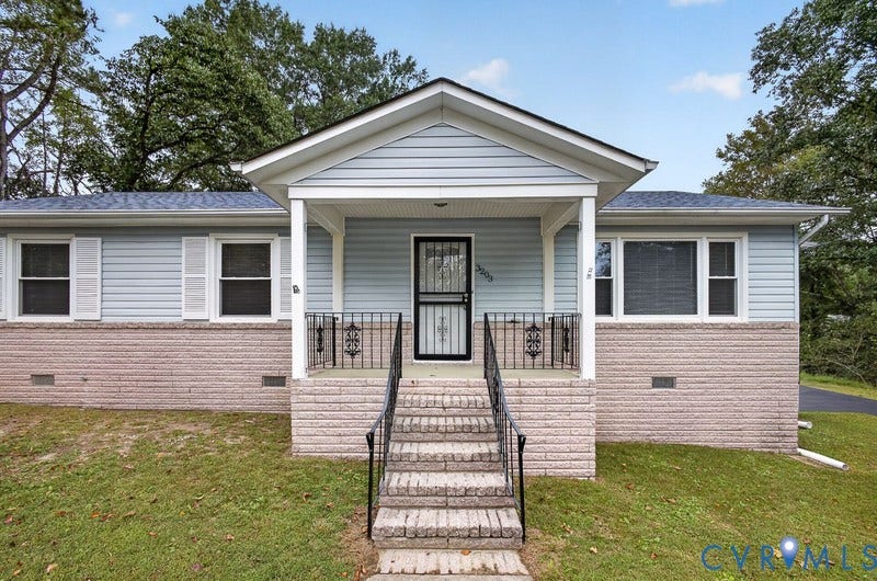Exterior featuring light blue horizontal siding, a masonry lower facade, a covered front porch with iron railings, and a shingled gable roof