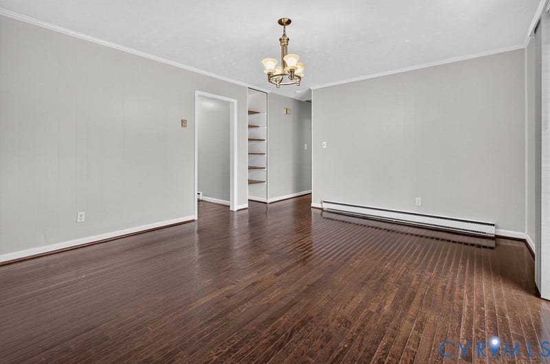 Interior space featuring dark wood-finish flooring, a multi-arm metallic chandelier, neutral wall tones, and open built-in shelving