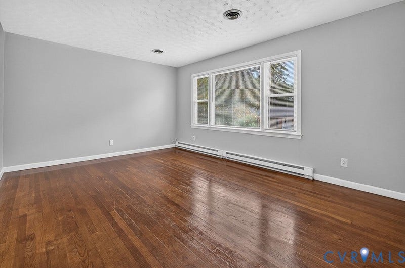 Spacious room featuring wood-finish flooring, large multi-pane windows, and neutral wall tones