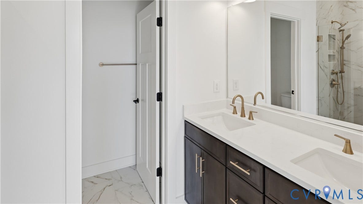 11612 Switch Drive, Midlothian Depot, Midlothian, VA 23113 Double vanity featuring dark cabinetry, quartz countertops, dual under-mount sinks with brass-tone fixtures, and a walk-in shower with stone-finish tile surround