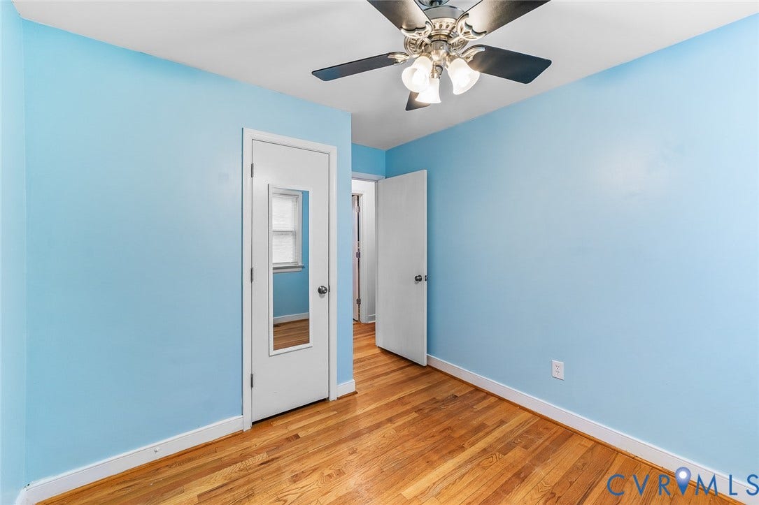 Interior room featuring wood-finish flooring, a ceiling fan with multi-light fixture, and a door with an integrated mirror