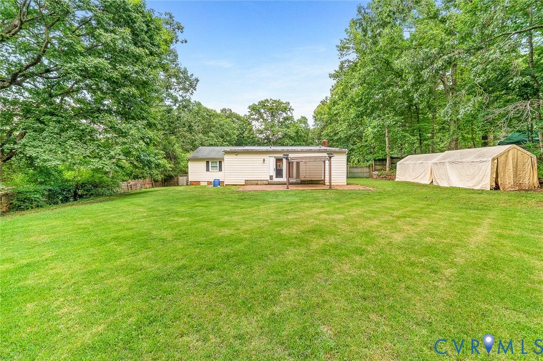 Expansive backyard featuring a level lawn, mature trees, a brick patio, and a wooden pergola