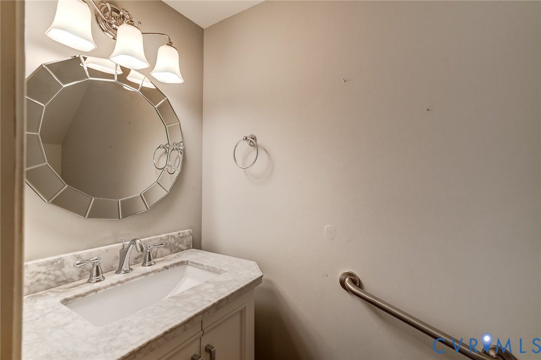 1109 Lakeland Circle, Henrico, VA 23229 Vanity featuring a stone-composite countertop with an integrated rectangular basin, three-light polished chrome fixture, decorative circular multi-faceted mirror, and metal wall-mounted grab bar