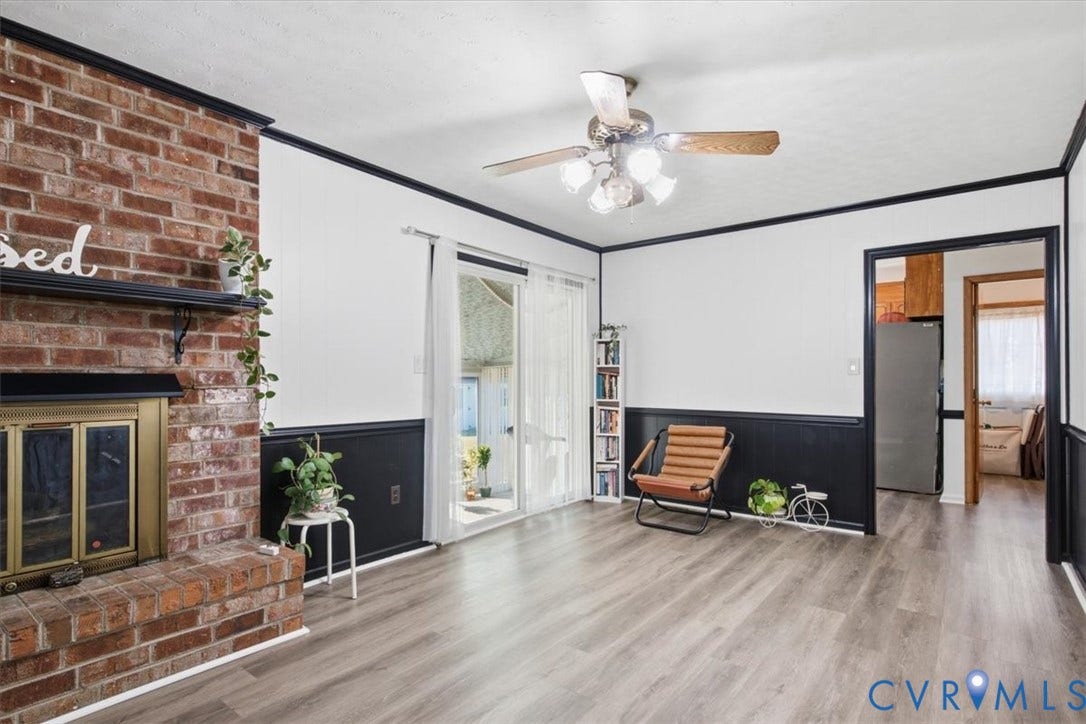 2609 Maury Road, Prince George, VA 23805 Full-height red brick fireplace featuring a metal fire screen and mantel, wood-finish flooring, dark wainscoting, sliding glass door, and a ceiling fan with multi-light fixture