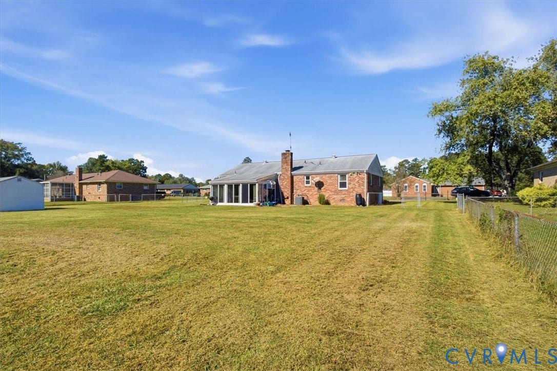 2609 Maury Road, Prince George, VA 23805 Expansive backyard featuring a large grass lawn, chain-link perimeter fencing, brick exterior construction, rear-facing chimney, and glass-enclosed porch