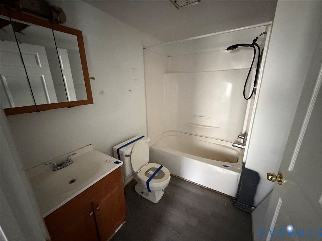 334 S 17th Avenue, Hopewell, VA 23860 Bathroom featuring a wood-finish vanity with an integrated sink, a medicine cabinet with mirrored doors, a standard toilet, and a bathtub-shower combination with a flexible handheld fixture on a tiled surround