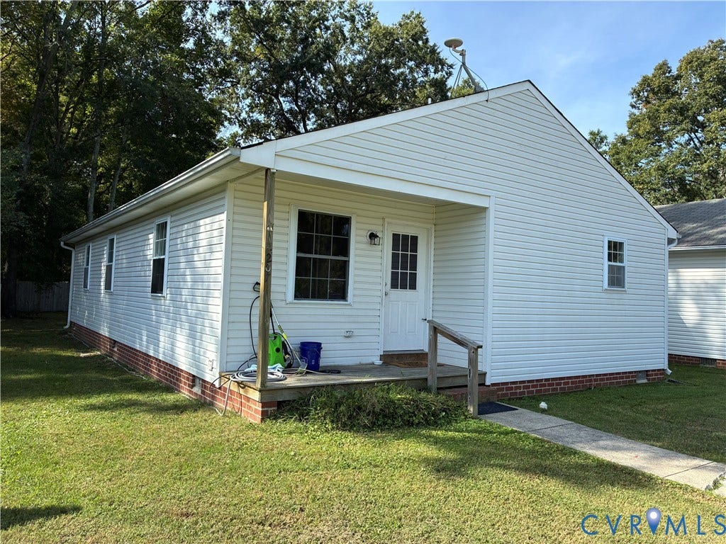 Vinyl siding exterior featuring a red brick foundation, covered porch with wooden support posts, and concrete walkway