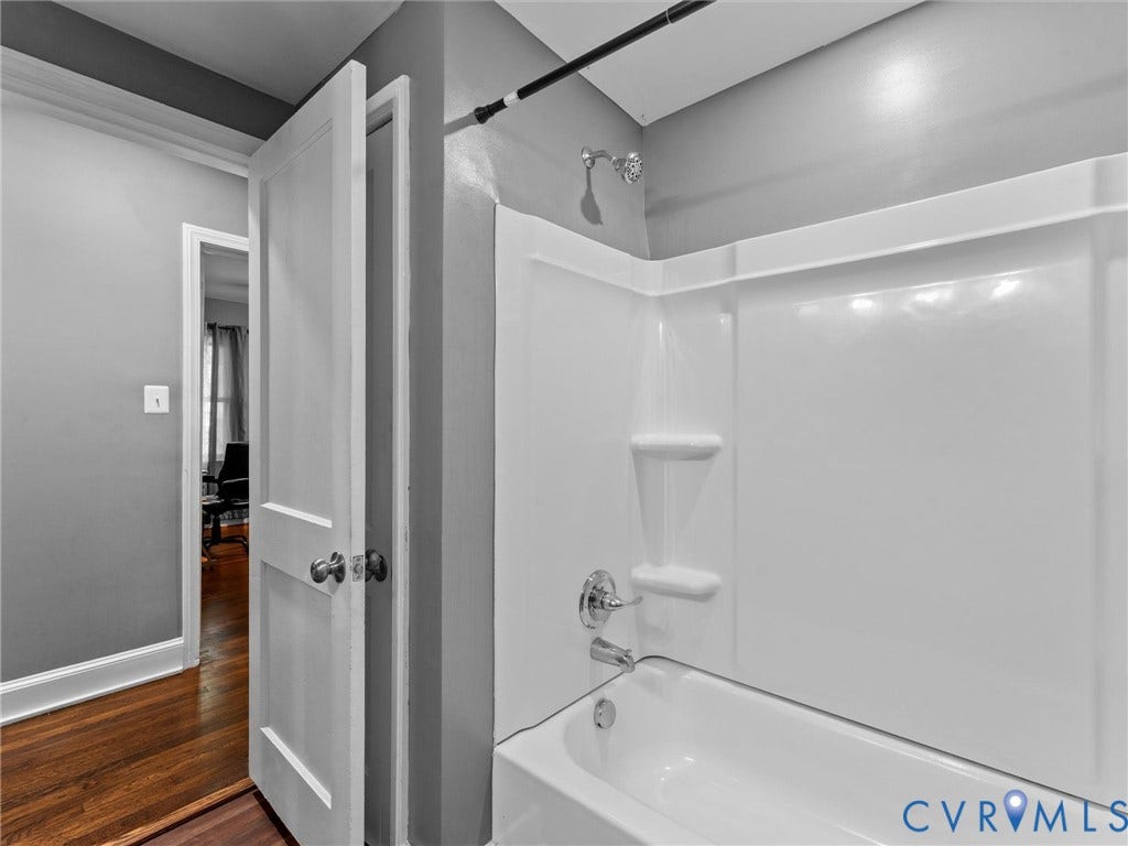 Bathroom featuring a white molded tub-and-shower surround with integrated shelving and chrome fixtures, complemented by hardwood flooring