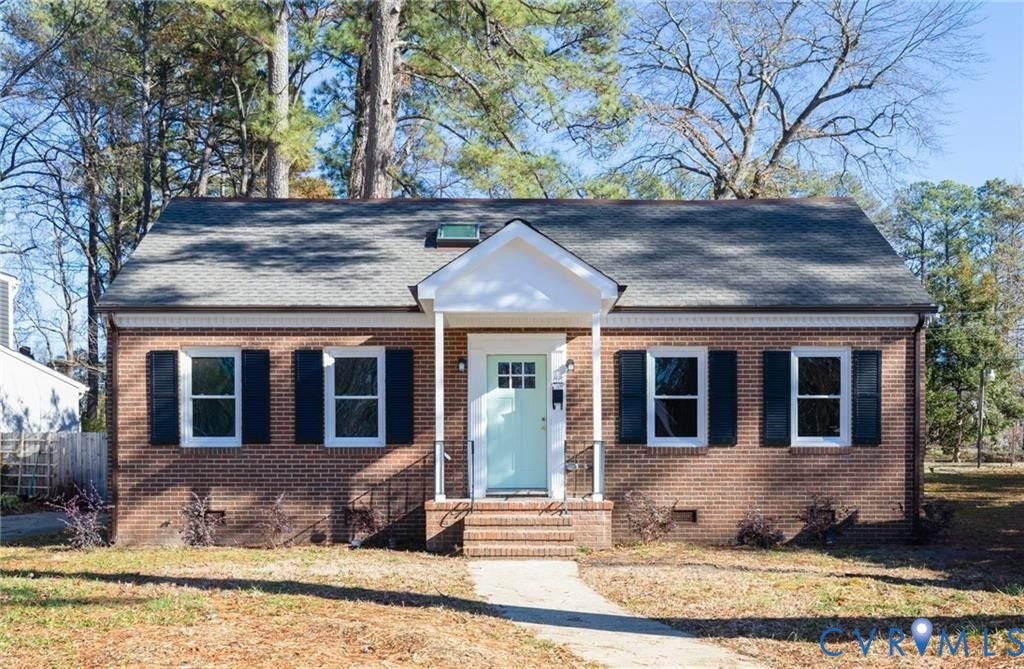 Brick exterior facade featuring a covered front entry, gabled roofline, symmetrical window placement, and dark shutters