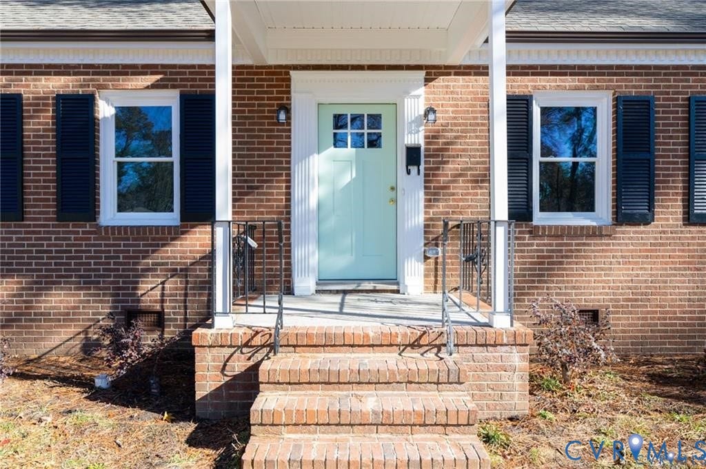 Brick exterior featuring a covered front porch, tiered brick steps, wrought iron railings, and shuttered windows