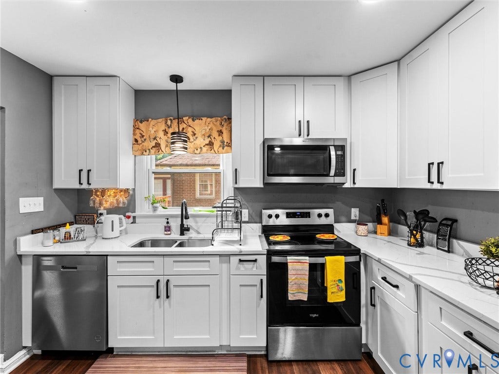 Kitchen featuring white shaker-style cabinetry, solid-surface countertops with grey veining, stainless steel appliances, and a dual-basin undermount sink with a matte black faucet