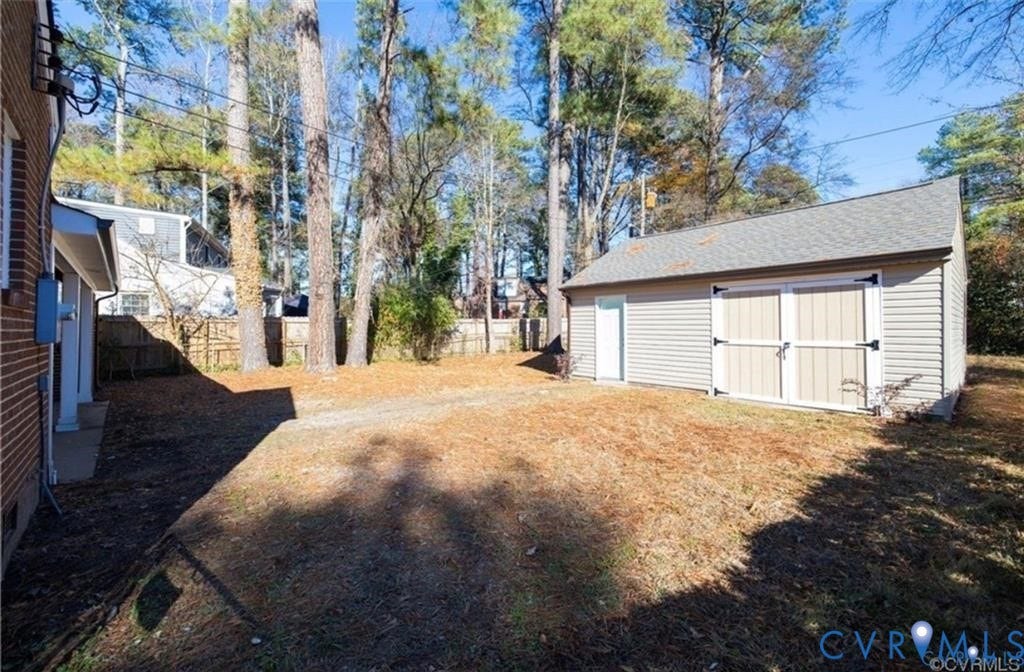 Backyard area featuring a detached outbuilding with double doors, mature trees, and perimeter wooden fencing