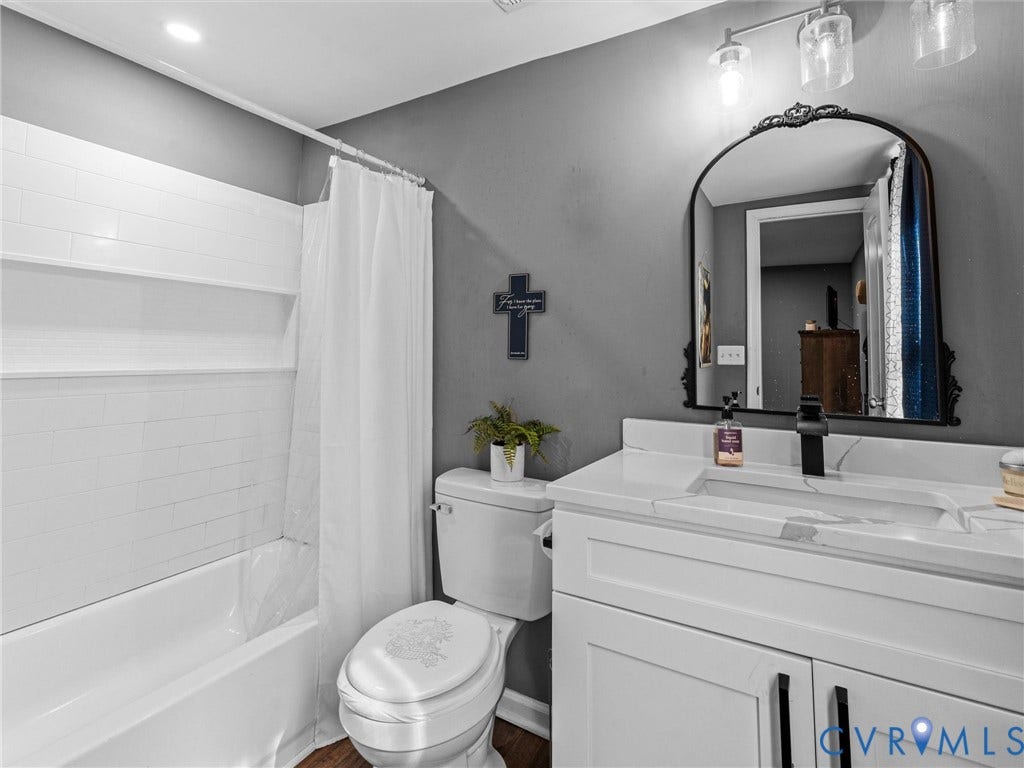 Bathroom featuring a white vanity with a stone countertop, an integrated rectangular sink, matte black faucet, and an arched wall-mounted mirror