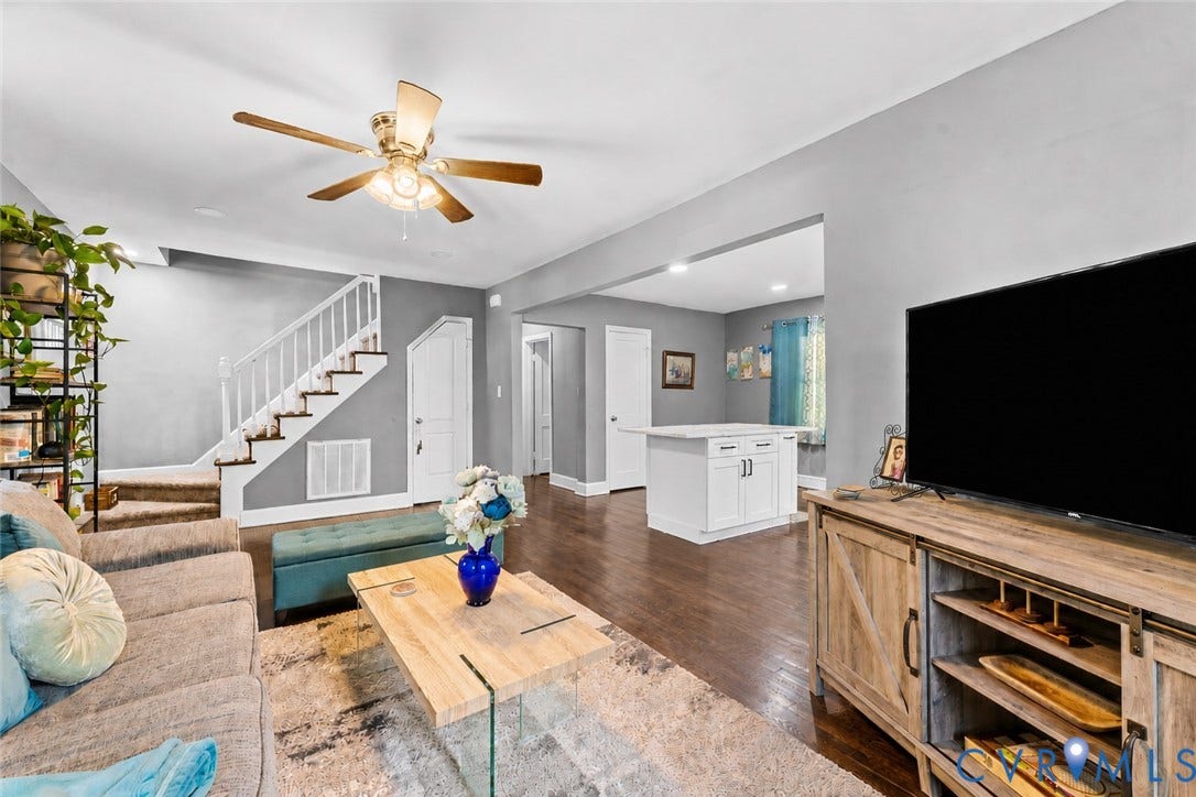 Living area featuring wood-finish flooring, a ceiling fan with integrated lighting, and a staircase with white balusters