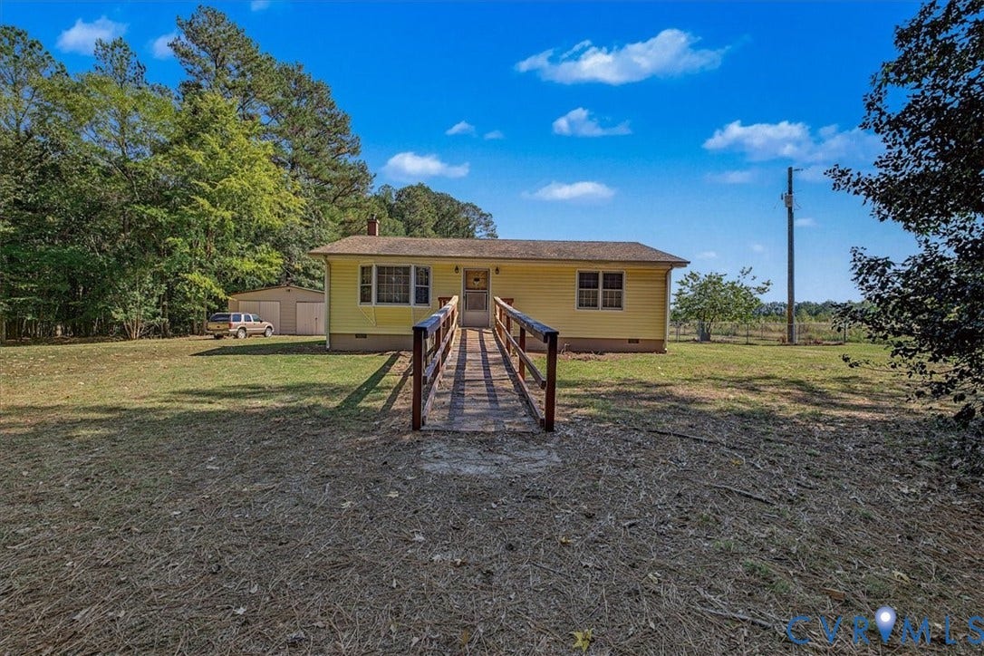 14421 Alden Road, Disputanta, VA 23842 Single-story residence with yellow siding, shingled roof, exterior accessibility ramp, detached garage, and mature tree-lined grounds