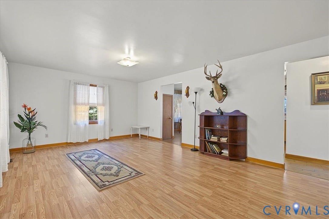 14421 Alden Road, Disputanta, VA 23842 Living area featuring wood-finish flooring, a built-in wooden shelving unit, wall-mounted sconces, and a flush-mount ceiling light fixture