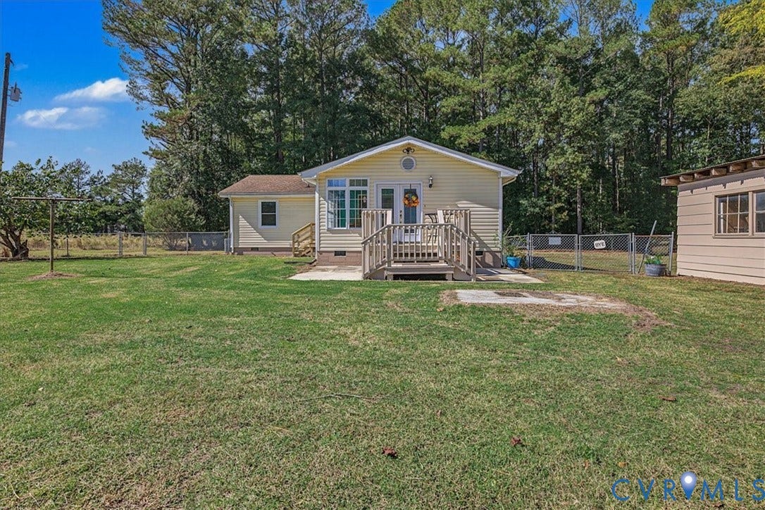 14421 Alden Road, Disputanta, VA 23842 Expansive backyard featuring a manicured lawn, perimeter chain-link fencing, mature tree backdrop, elevated wooden deck with stairs, and an attached auxiliary structure