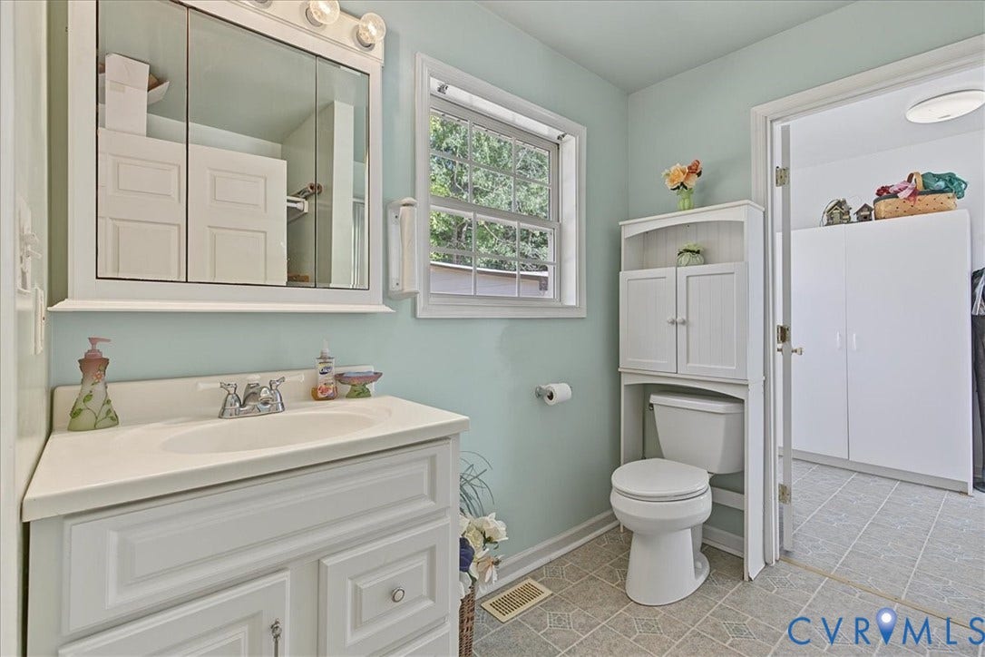 14421 Alden Road, Disputanta, VA 23842 Bathroom featuring a white vanity cabinet with a solid surface countertop, an integrated sink basin, a multi-panel mirrored medicine cabinet with integrated lighting, a single-hung window, and tile flooring