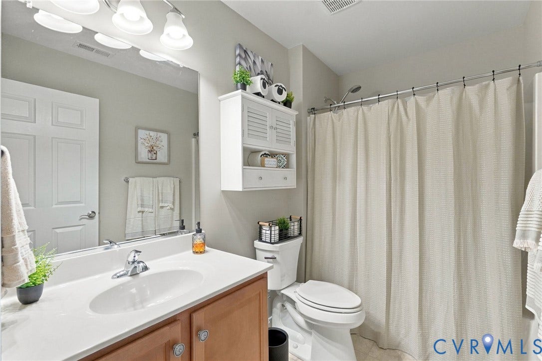 8146 Janice Avenue, Mechanicsville, VA 23111 Bathroom featuring a wood-finish vanity with a solid-surface countertop, an oval undermount sink, built-in white cabinetry, and wall-mounted vanity lighting