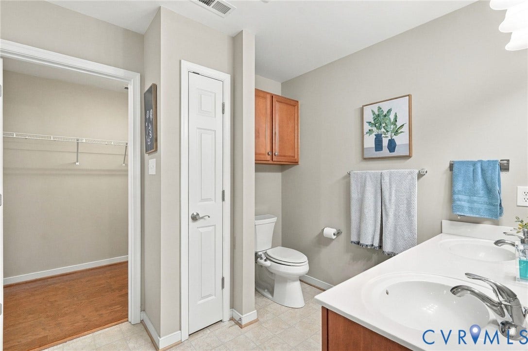 8146 Janice Avenue, Mechanicsville, VA 23111 Dual-sink vanity with white countertop, wood-finish cabinetry, wall-mounted storage cabinet, and walk-in closet featuring built-in wire shelving