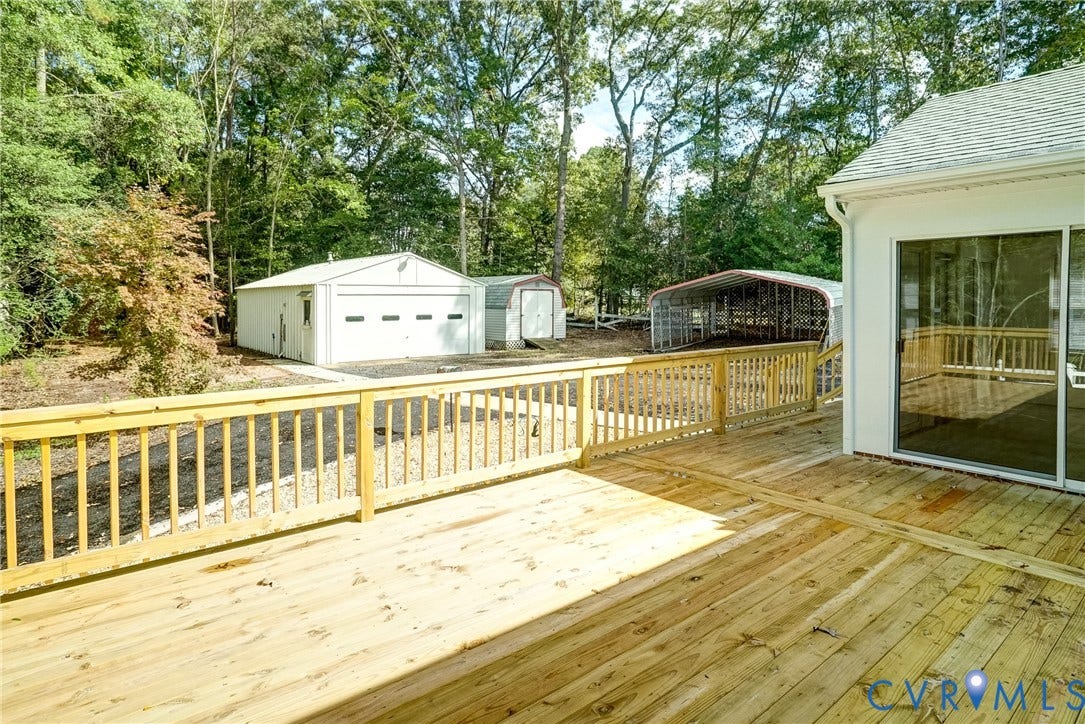 4130 Charles City Road, Charles City, VA 23231 Elevated wood deck featuring a balustrade railing, detached garage, and exterior storage structures situated on a wooded lot
