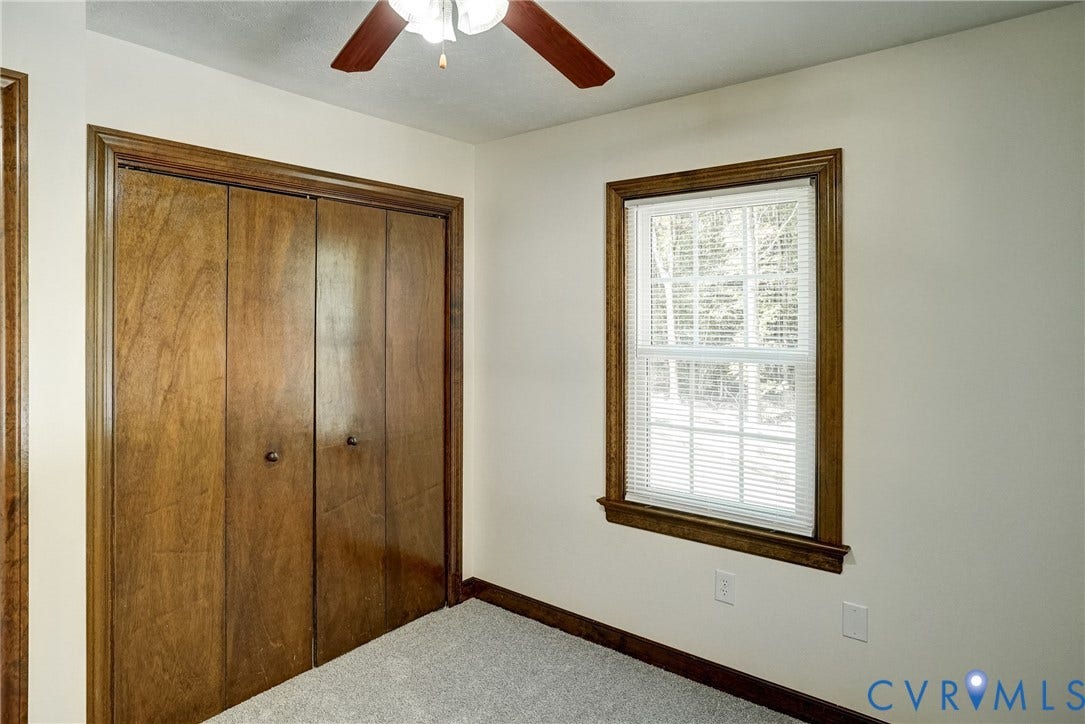 4130 Charles City Road, Charles City, VA 23231 Neutral-toned room featuring a wood-trim window, wall-to-wall carpeting, wood-finish bi-fold closet doors, and a ceiling-mounted fan with light fixture