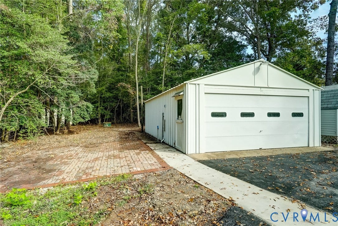 4130 Charles City Road, Charles City, VA 23231 Detached metal-sided garage featuring a sectional garage door with windows, side-entry door, paved brick exterior surface, and asphalt driveway