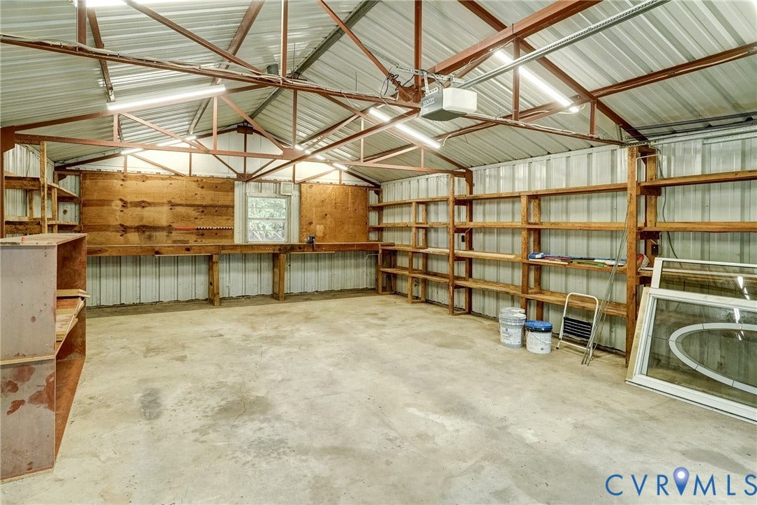 4130 Charles City Road, Charles City, VA 23231 Workshop area featuring exposed metal truss ceiling, concrete flooring, extensive wood-frame built-in wall shelving, and a wood-surfaced workbench