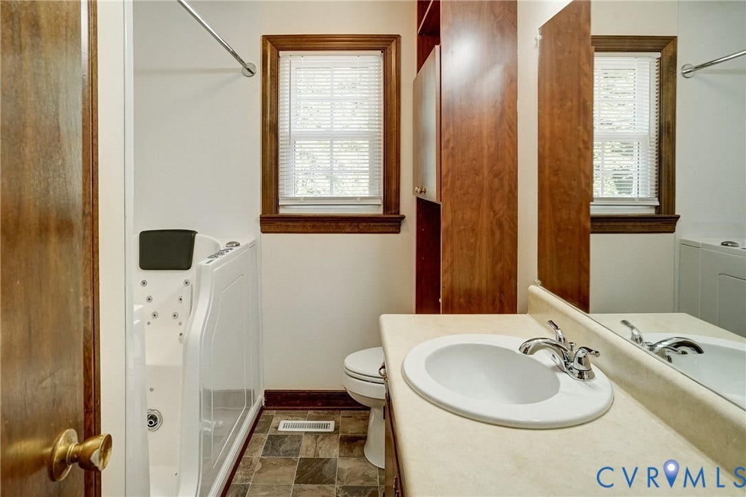 4130 Charles City Road, Charles City, VA 23231 Bathroom featuring a walk-in jetted tub, stone-finish tile flooring, built-in floor-to-ceiling cabinetry, vanity with a molded countertop, and wood-trim window casing