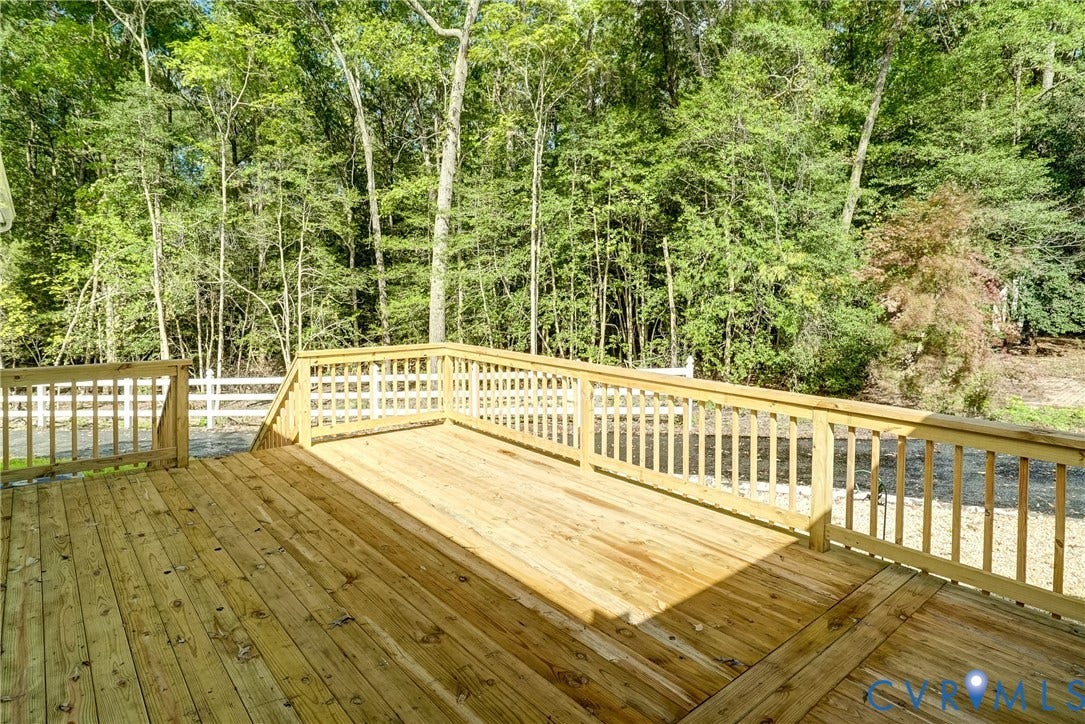 4130 Charles City Road, Charles City, VA 23231 Elevated wooden deck featuring vertical baluster railings, lattice accents, and natural wood plank flooring, backing to dense mature trees