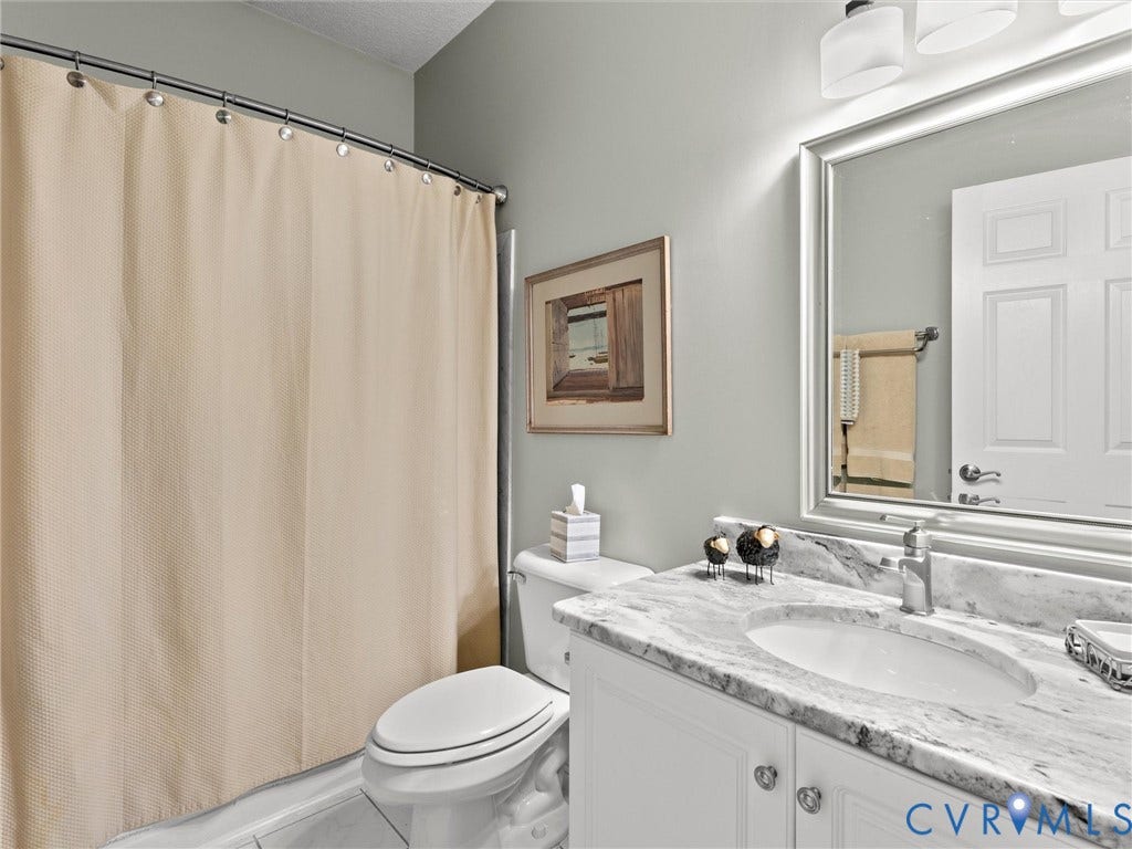 4105 English Holly Circle, Glen Allen, VA 23294 Bathroom vanity featuring stone-finish countertop, undermount sink, chrome-finish faucet, and white cabinetry, complemented by a large framed wall mirror and multi-bulb vanity light fixture