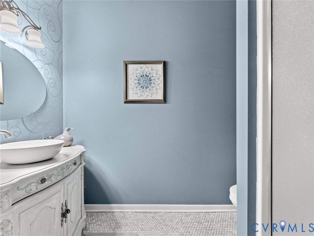 4105 English Holly Circle, Glen Allen, VA 23294 Vanity featuring a white cabinetry base with decorative detailing, a rounded vessel sink, and a multi-light wall fixture above an oval mirror